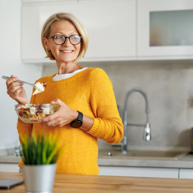 Attractive mature woman eating salads in her kitchen.Mature woman eating salads at home.